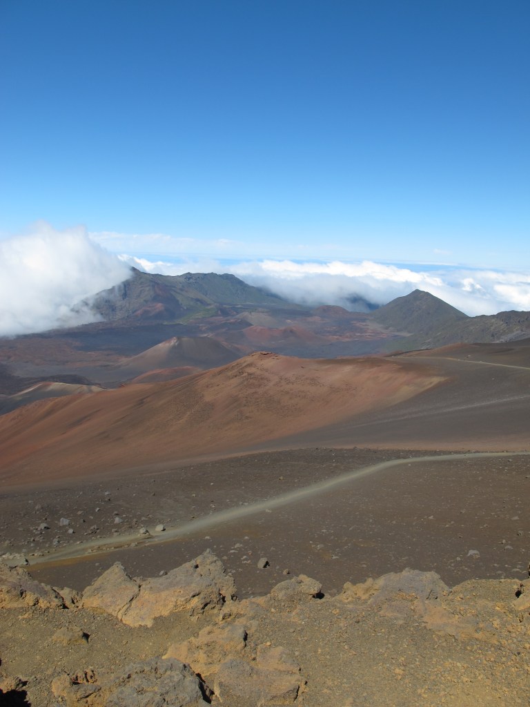 Blick vom Haleakala, dem höhstem Berg auf Maui, Hawaii auf eine vulkanische Mondlandschaft. Das es nicht der Mond ist erkennt man an den tiefer liegenden Wolken und dem blauen Himmel (von Ronny Errmann)